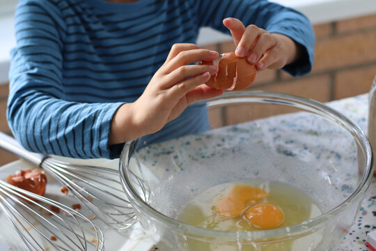 Child broke fresh egg. Child hand crack egg for cooking, baking cake, waffles at home in the kitchen. Fresh free range eggs in a glass bowl. Close up photo family lifestyle.