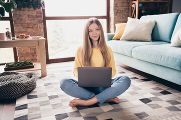 Full body photo of teenager barefoot girl using netbook when learning it courses sitting floor...