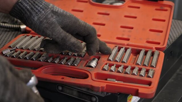 A close-up of a man selects the right screwdriver attachment in a professional tool kit at a service station. A set of professional tools for car repair. Car service station.