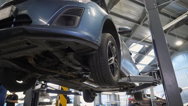 A blue car that is lifted on a lift before being inspected at a service station. Checking the condition of the car during a visit to the master. A passenger car is lifted on a car lift.