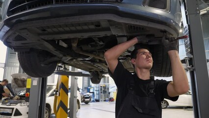 An auto mechanic working under the car on a car lift in the garage, he disassembles the bottom of the car for further repair. Antifreeze drain in the service station. Auto repair shop, auto repair.