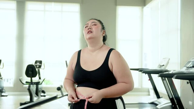 Chubby woman Exercise in fitness using a tape measure around waist. Face disappointed at not being able to lose weight to make waist smaller After running on the treadmill in attempt to lose weight
