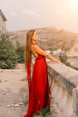 Woman red dress. Summer lifestyle of a happy woman posing near a fence with balusters over the sea.