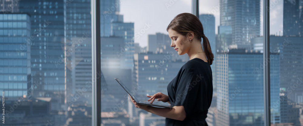 Poster caucasian businesswoman standing in her corner office next to big window with city view and using la
