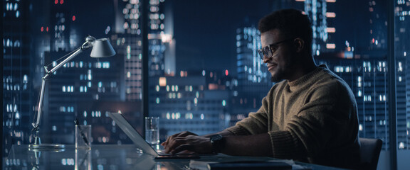 Successful Handsome Black Businessman Working on Laptop Computer in Big City Office in the Evening....