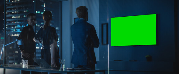 Modern Skyscraper Office Late At Night: Male And Female Caucasian Business Partners Watching Green...