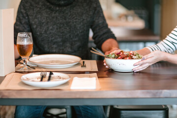 Waitress serving a salad plate to a man with a beer at a wooden table in a restaurant