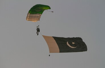 Active male soaring through the sky attached to a parachute with a Pakistan flag in the wind