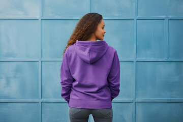 rear view of Young brunette woman in purple violet hoodie on blue modern background copy space...