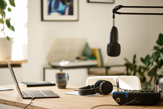 Microphone hanging over desk with headphones, soundboard and laptop which is workplace of radio presenter or podcast creator