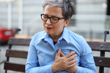 Senior woman, experiencing chest pain, signifies a potential cardiac issue, invoking concern for her health. - obrazy, fototapety, plakaty