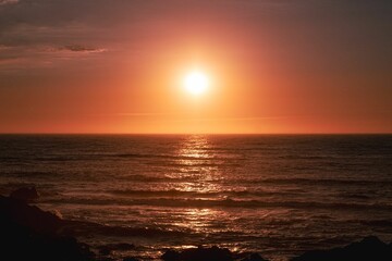 Obraz premium Scenic view of sea waves reflecting a red sunset