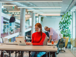 Obraz premium In a modern startup office, a professional businesswoman with orange hair sitting at her laptop, epitomizing innovation and productivity in her contemporary workspace