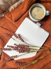 The image shows a notebook, cup of coffee, and flowers on a sweater. 
