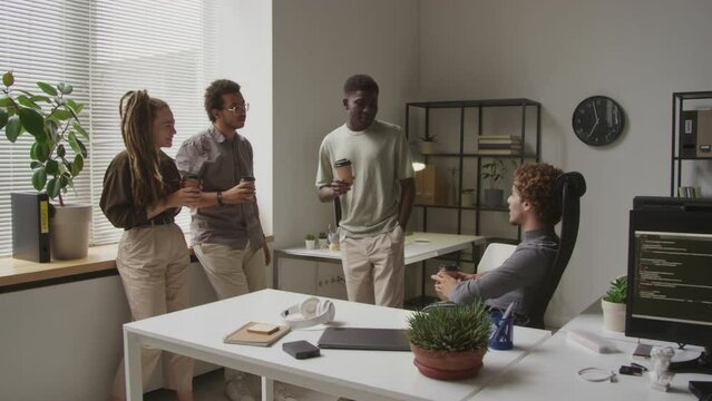 Four multiethnic male and female co-workers chatting during coffee break in contemporary programmers office
