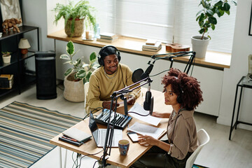 Young African American woman speaking in microphone during podcast or interview with invited guest...