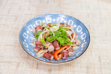 Squid tentacle salad, cut into pieces. Squid salad, Thai style, sour, spicy, delicious. Squid salad on a white plate.