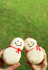 Hands Clinking Adorable Snowman Shaped Doughnuts on Blurry Lawn