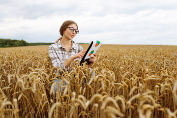 Naklejka na ściany i meble Young female farmer checking crop growth with clipboard in golden wheat field. Smart farming. Agribusiness.