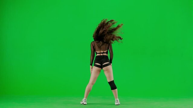 Framed on a green background, chromakey stands a young woman. She looks into the camera, wears outspoken clothes and demonstrates the Twirk dance. Shes sexy, plastic
