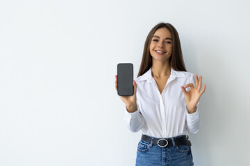 Naklejka premium Beautiful young woman with mobile phone showing OK on white background
