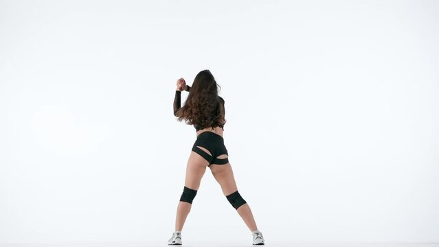 In the frame on a white background stands a young, slender woman. She is dressed in open clothes. Shows dance moves in twerk style, shakes buttocks, jumps. Shes sexy, plastic, rhythmic. Slow mo