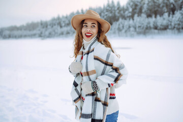 Fototapeta na wymiar Beautiful young woman with red lips wearing a hat and a light scarf enjoys a winter day in a snowy forest. Happy female tourist posing outdoors. Christmas.