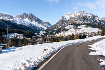Road leading to a mountain village surrounded by towering peaks covered in snow in winter