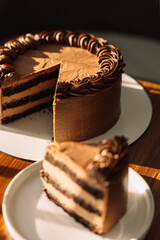 Cut puff chocolate piece from a cake on a white plate on a wooden table under the morning sunlight.