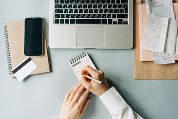 Top view of an unrecognizable woman working and writing goals in notes on office desk.