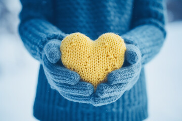 Fragment. The hands of a girl in a blue sweater holds a knitted heart against the background of falling snow