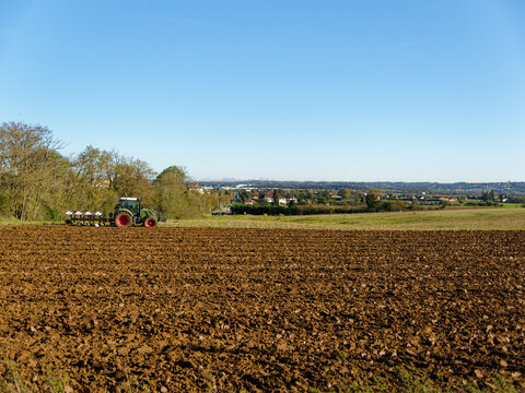 Tractor plowing a field in autumn, earth is brown and freshly plowed, blue sky, distant alps in the background, Corbas, France