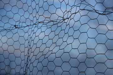Chain-link fence fragment. fine twisted wire isolated on blue cloudy sky background. Secured...