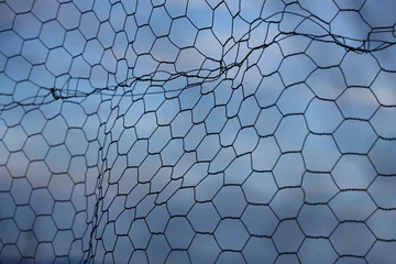 Foto op Plexiglas Chain-link fence fragment. fine twisted wire isolated on blue cloudy sky background. Secured territory, protected area fencing. © Maxim Chuev