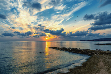 Colorful sunset on the Black Sea. Sea breakwaters. Sunset over the sea with waves. Seascape at sunset under a cloudy sky. Waves on the sea and dark clouds in the blue sky.