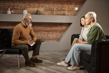 Obraz premium lesbian couple talking to bearded middle aged psychologist in glasses during therapy session