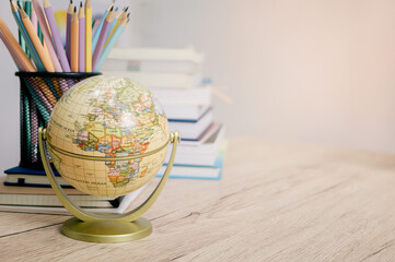 Education concept featuring globes, colorful pencils, pens, and books on a modern table against a...