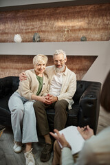 happy married middle aged couple hugging and sitting on leather couch during family therapy session