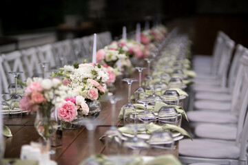 A large, long, decorated, wooden table and chairs, covered with a white tablecloth with dishes, flowers, candles.