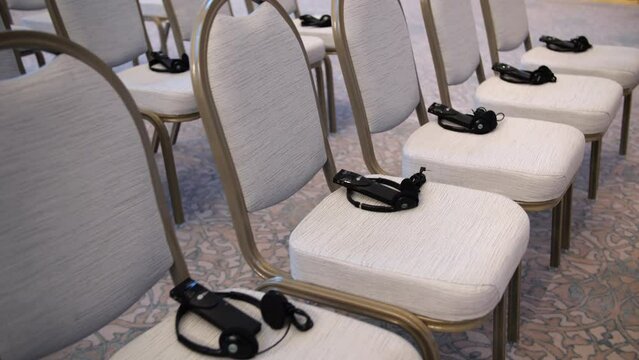 Simultaneous translation headsets lie on chairs in the conference room before the start of a press conference. Equipment for simultaneous translation at a meeting.