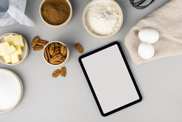 Digital touch screen tablet with brownie recipe ingredients and kitchen utensils on gray...