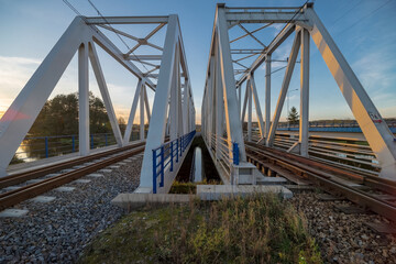 Dwudzielny stalowy most kolejowy o ażurowej konstrukcji w porze zachodu słońca w listopadowe popołudnie nad rzeką Kamienną . - obrazy, fototapety, plakaty