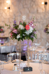Centerpiece made of green leaves and fresh flowers stands on the dinner table. Wedding day.