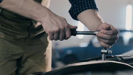 Hands of an auto mechanic close-up working on a car engine in a car repair shop. Ratchet wrench
