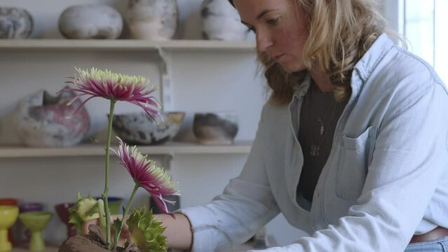 Witness the enchanting process of artistic creation as a skilled female ceramicist works her magic in a luminous workshop. Positioned before a table adorned with scattered materials and tools, she