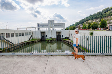 Smiling female tourist together with her dachshund standing in front of Lanaye lock against gray...