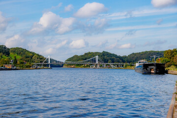 Albert canal and Kanne vehicular suspension bridge, mountains with green trees against blue sky and...