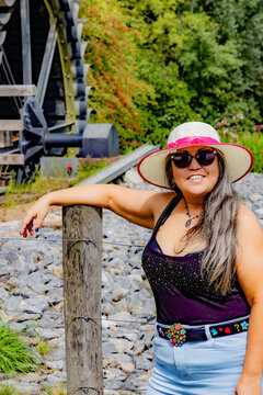 Happy smiling female tourist in hat and sunglasses, looking to camera, old Eper or Wingbergermolen water mill in blurred background, sunny day in Terpoorten, Epen, South Limburg, Netherlands