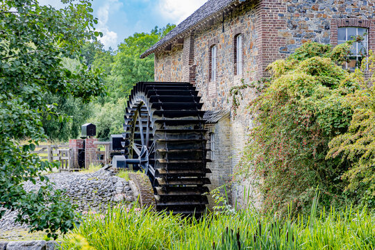 Old Eper or Wingbergermolen water mill next to stone building, Geul river, wild vegetation and trees in background, sunny day in Terpoorten, Epen, South Limburg, Netherlands