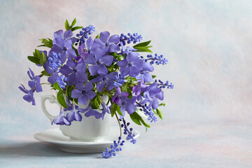 Bouquet with spring blue and purple flowers in a cup, periwinkle, muscari, violets on a light background, copy space